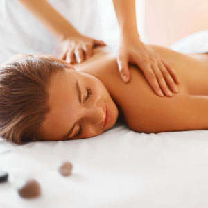 Foto a color de una mujer rubia recibiendo un masaje relajante. Se ven las manos de la terapeuta apoyada en su espalda