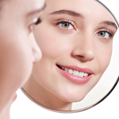 Rostro de una mujer joven mirándose en el espejo depués de un tratamiento facial