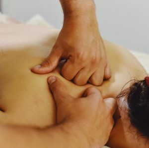 Mujer tumbada en una camilla con las mano de un terapeuta haciendo un masaje profundo de espalda en zona trapecio, romboidés