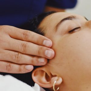 Una mujer esta recibiendo una masaje de cabeza. el terapeuta tiene sus dedos apoyados en cada lado de su cabeza