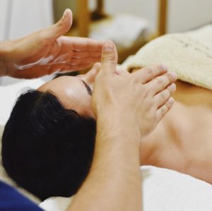 Mujer recibiendo una tratamiento y masaje de aromaterapia . Esta tumbada en una camilla y un terapeuta tiene la manos abiertas, y sostenidas encima de su nariz