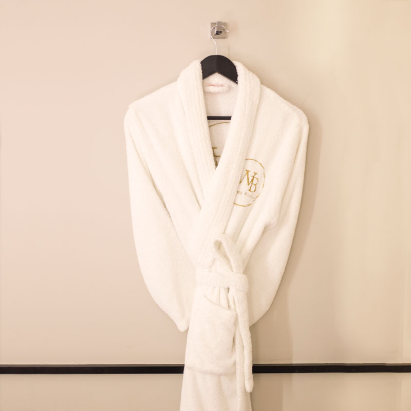 Albornoz blanco con Logo Dorado colgado sobre una percha negra en una cabina de tratamiento en Wellness Boutique Experience