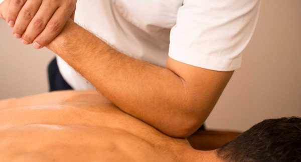 Foto de un cliente recibiendo un masaje tejido profundo en zona de espalda en Wellness Boutique. el terapeuta lleva una bata blanca y esta presionando los musculos romboides del con el codo