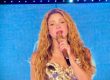foto de shakira en concierto 2026 en madrid, lleva un vestido dorado y el micrófono dorado en la mano izquierda, tiene el pelo suelto y ondulado
